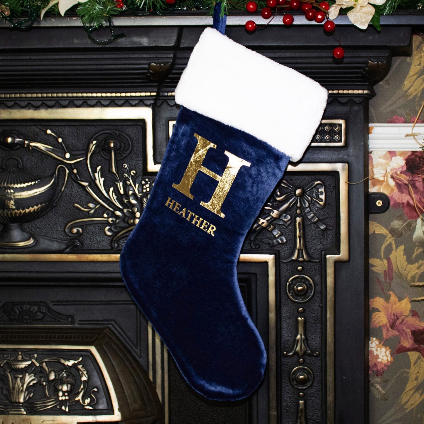 Navy Christmas stocking with gold 'H' and 'HEATHER' text, hanging on a decorative fireplace.