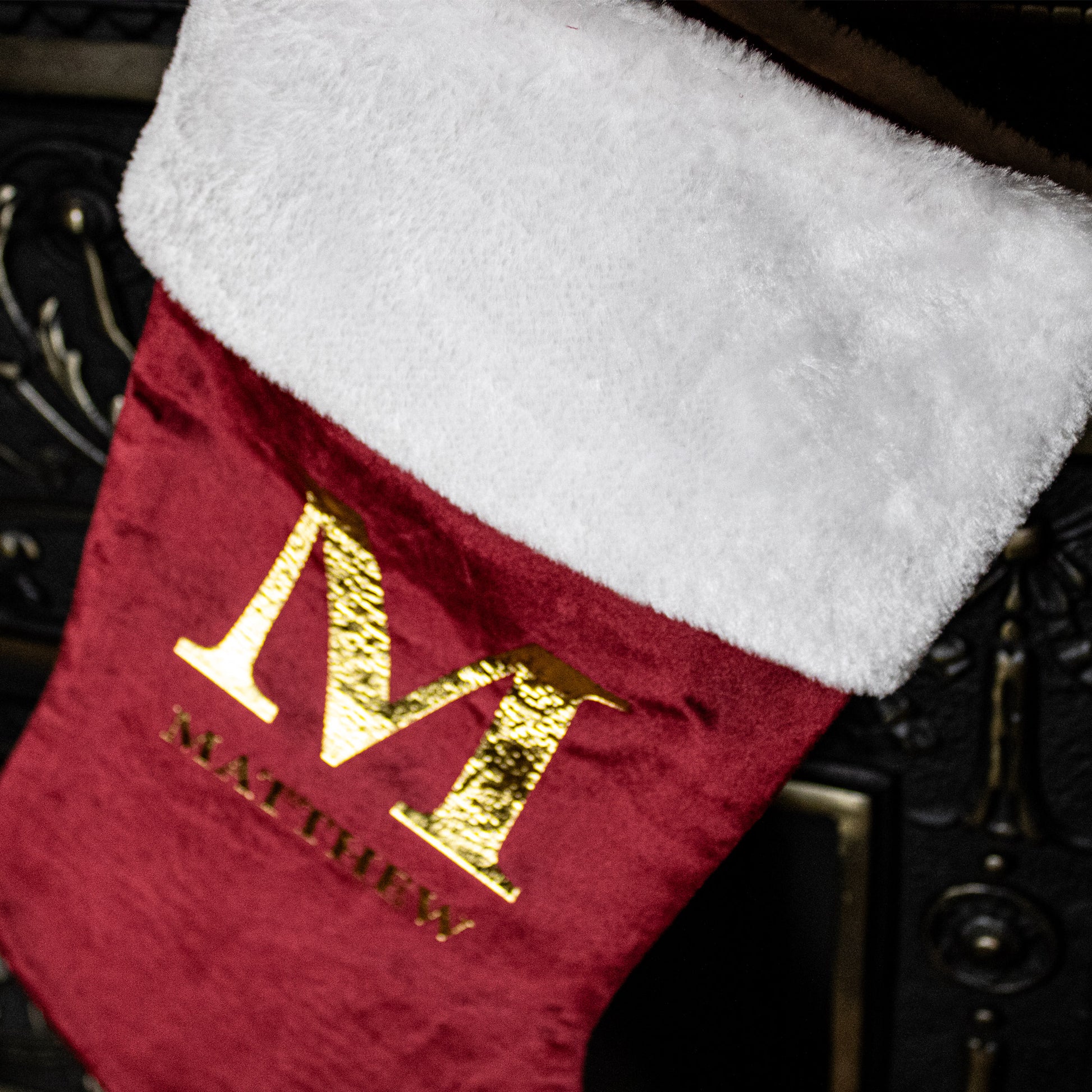Red Christmas stocking with gold letter 'M' and name 'MATTHEW' on a dark background