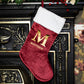 Red Christmas stocking with gold letter 'M' and name 'Matthew' on a decorative fireplace.
